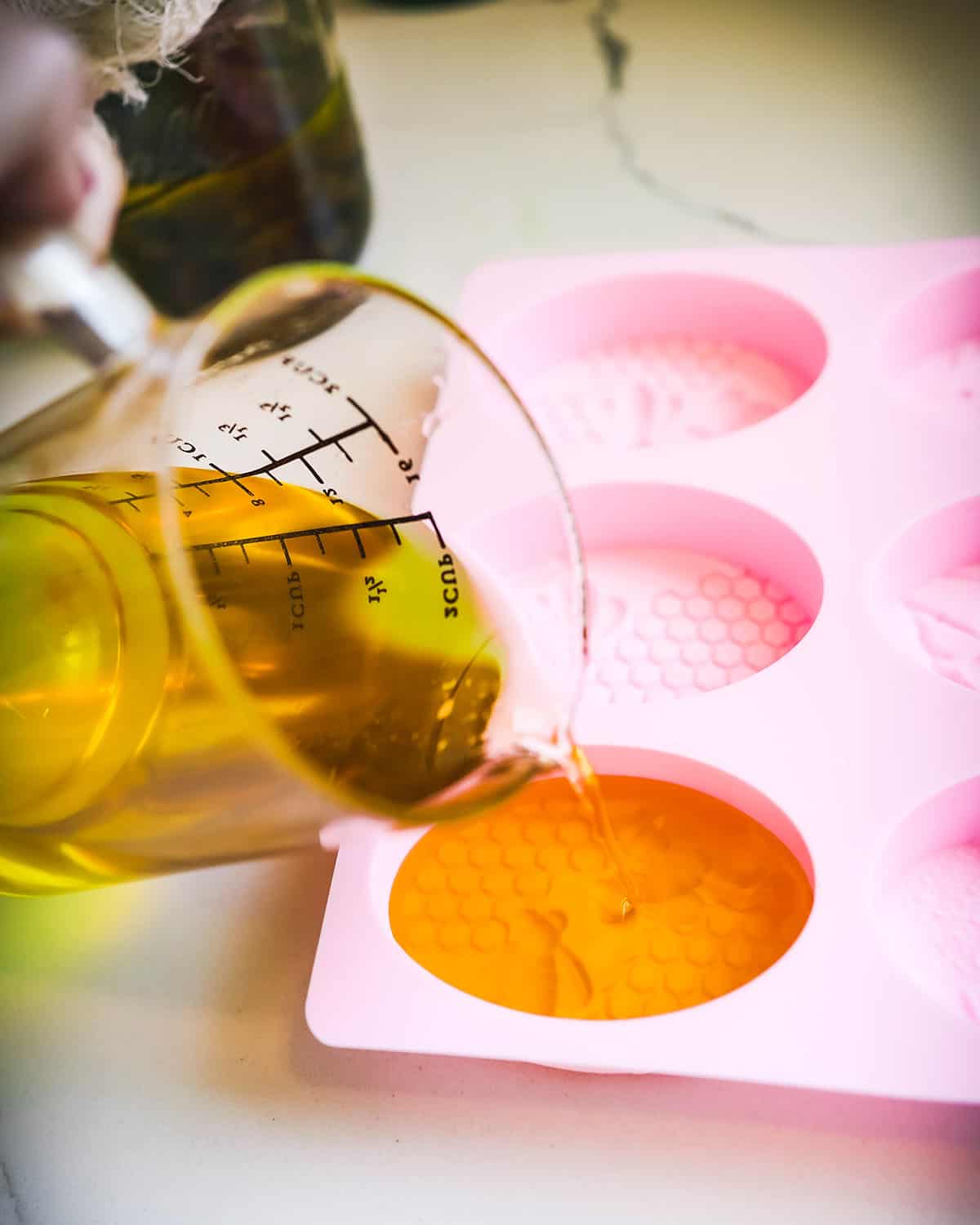 Melted wax and oils being poured into pink silicone molds. 