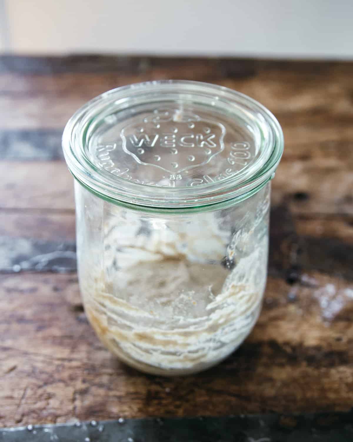 A jar with a glass lid, containing a not yet bubbling small amount of sourdough starter. 