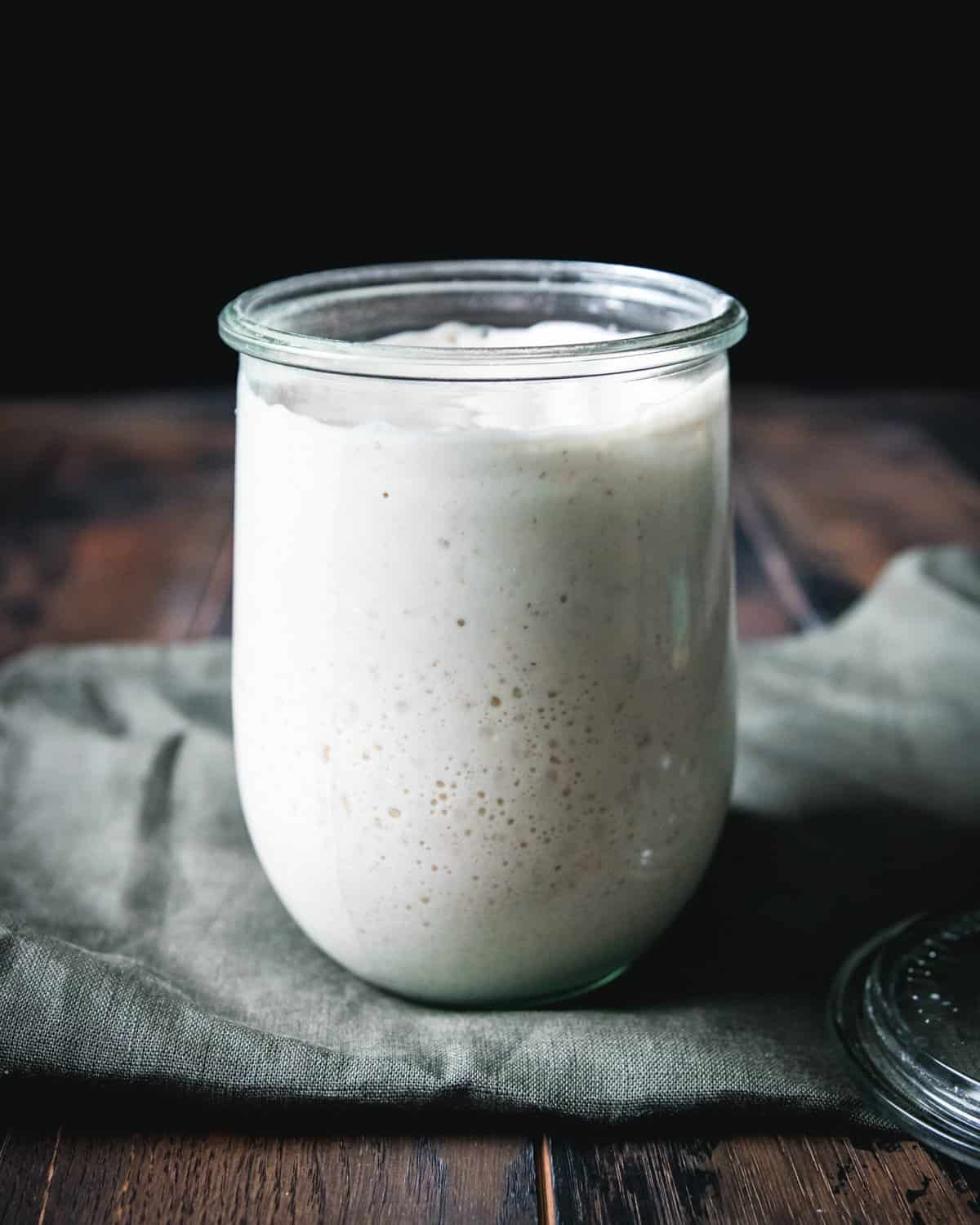 Sourdough starter in a jar ready to use, on a green cloth sitting on a dark wood background.