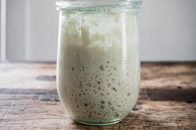 A jar of sourdough starter on a wood surface.