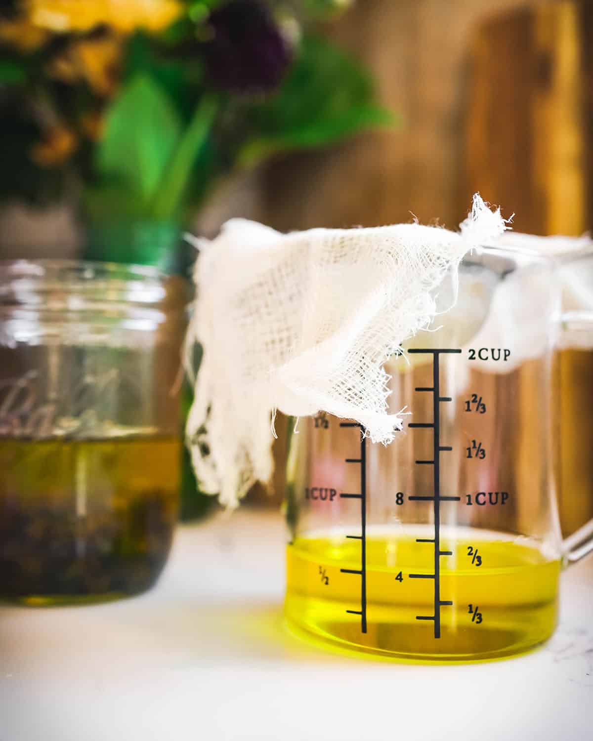 A jar of strained dandelion infused oil, with cheese cloth resting on top. 