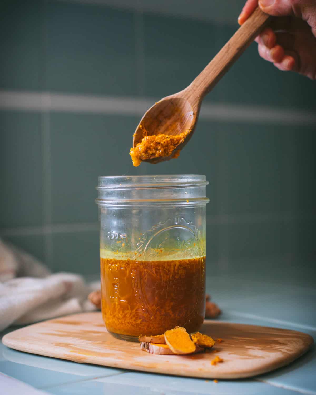 adding fresh grated turmeric root with a wooden spoon to the turmeric bug