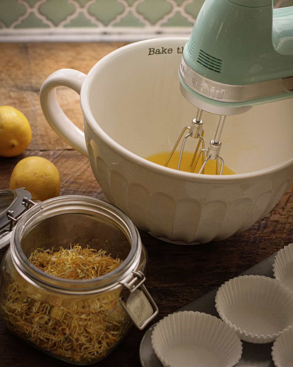 A mixer bowl with butter and sugar being mixed, with a jar of fresh dandelion petals ready to the side. 