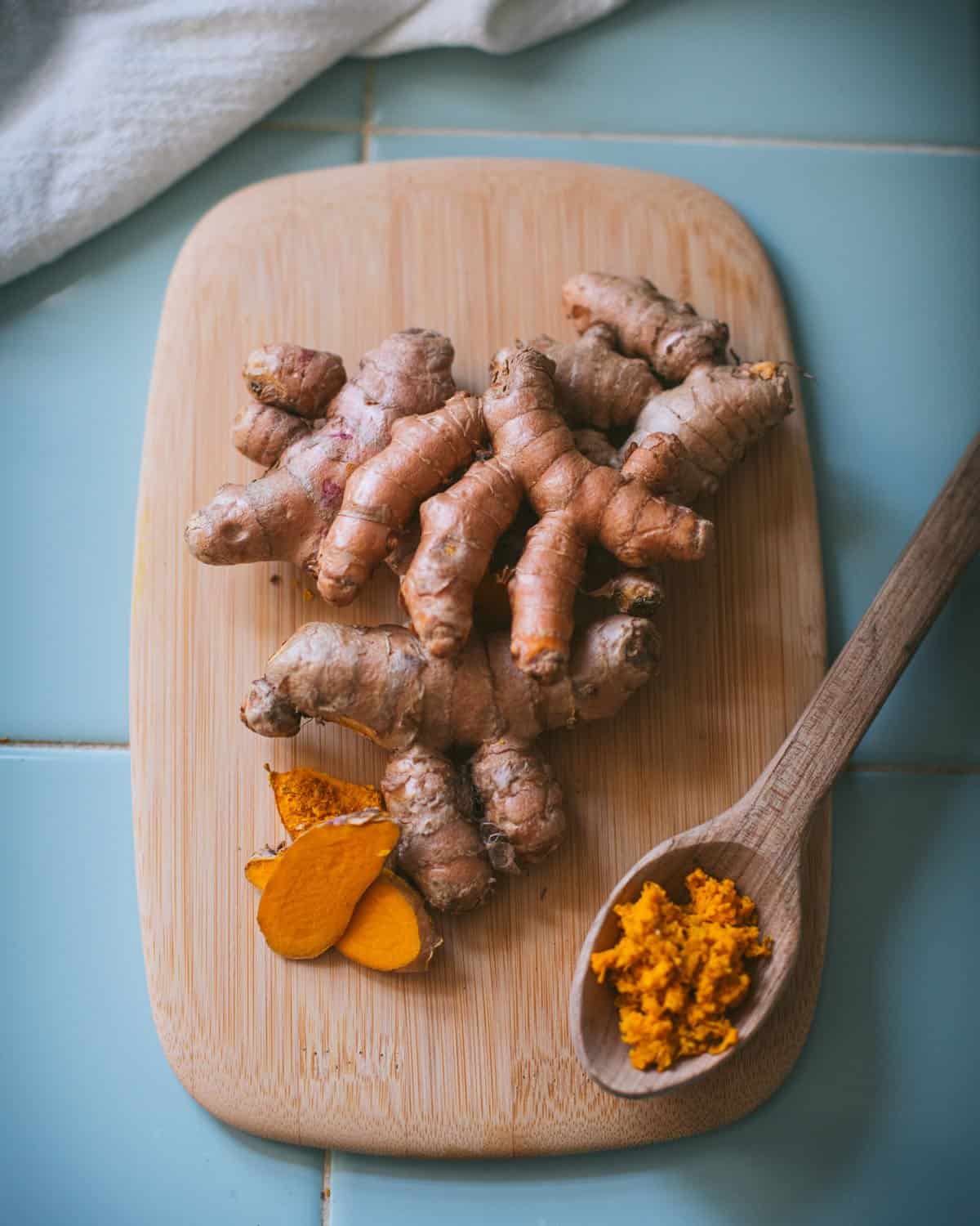 fresh whole, sliced, and grated turmeric root on a wooden cutting board