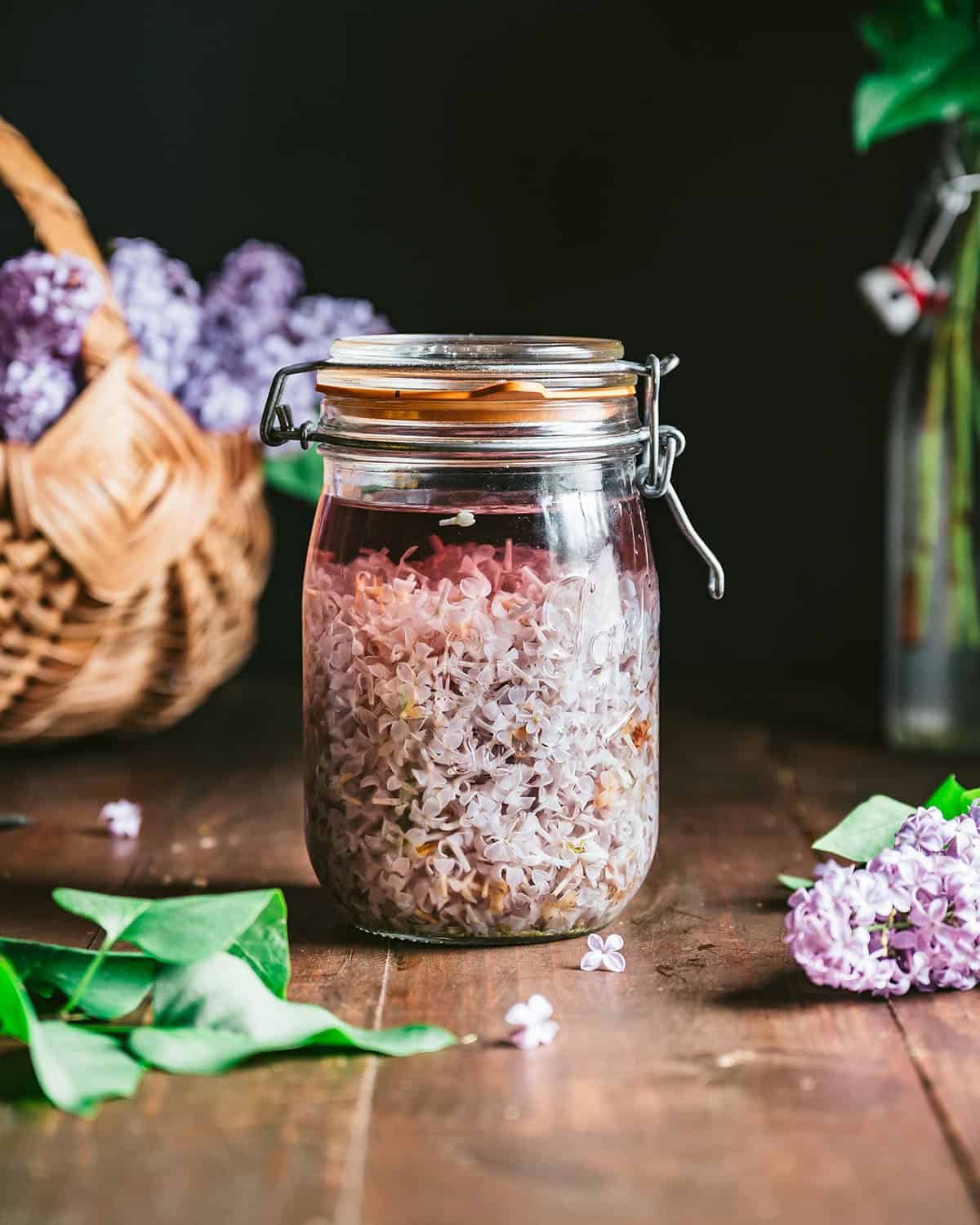 A closed jar of lilac flowers that are steeping in hot water, the water turning a lovely dark purple hue. 