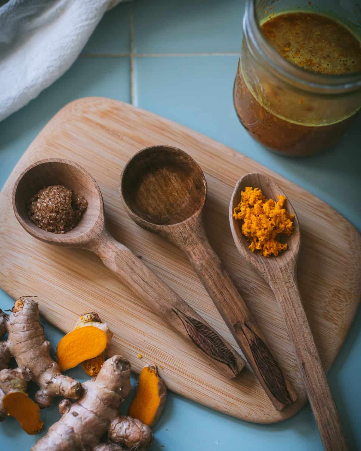 three wooden spoons with sugar, water, and grated turmeric root