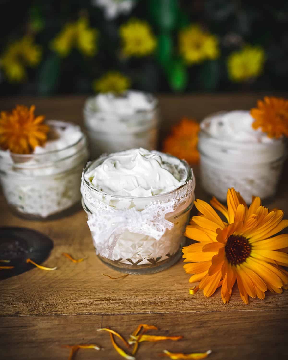 Whipped calendula body butter in small jars, surrounded by orange calendula flowers. 