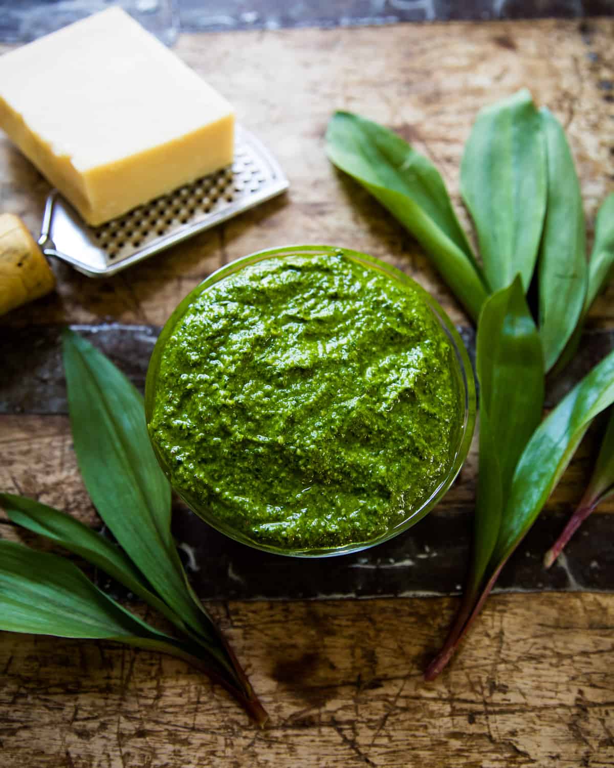 ramp pesto on a wooden table with ramp leaves and parmesan cheese