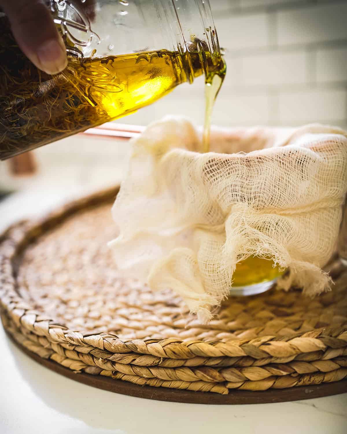 Straining the calendula infused oil with a strainer and cheesecloth into a bowl. 