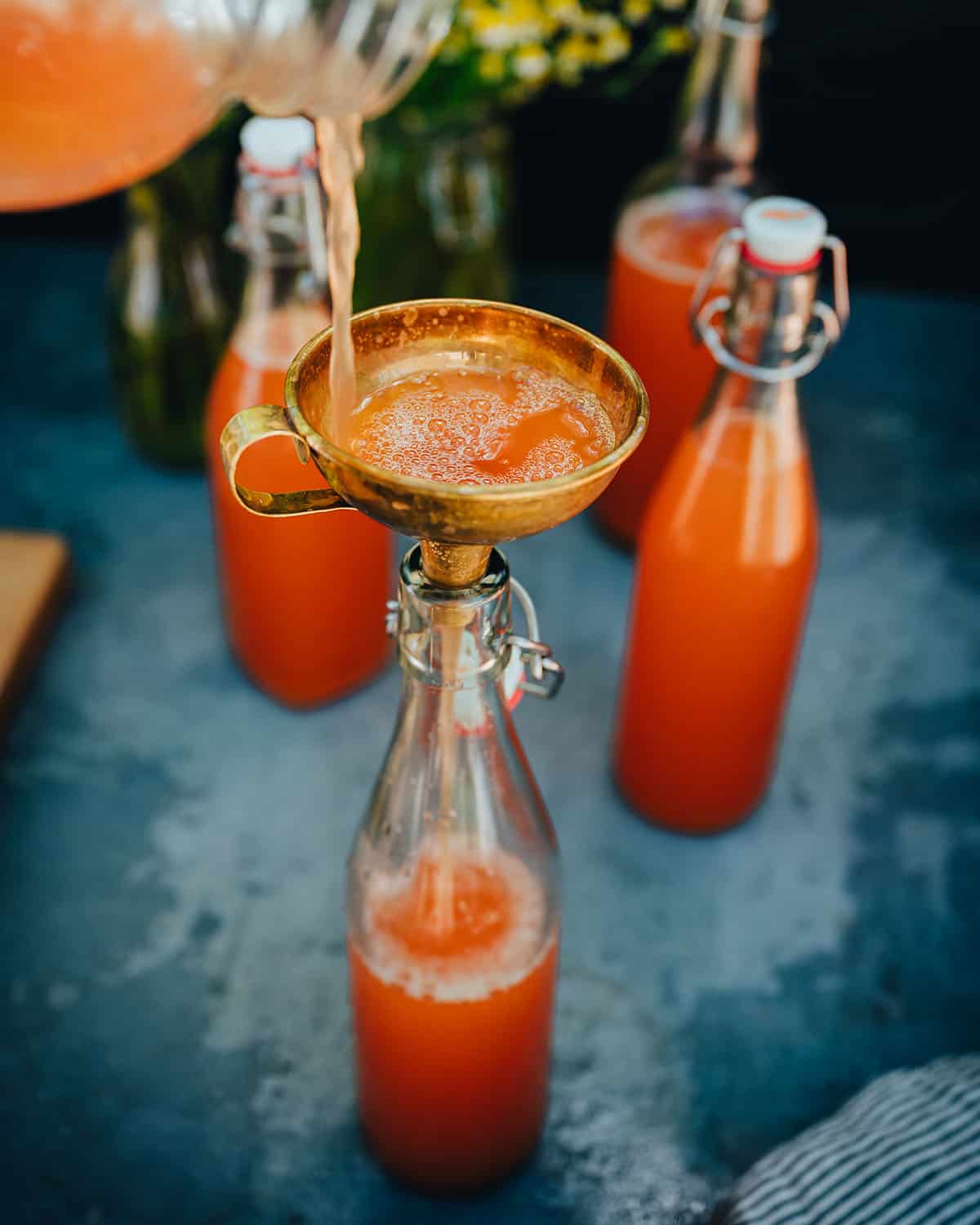 A funnel with yarrow rose soda pouring bottles with locking caps.