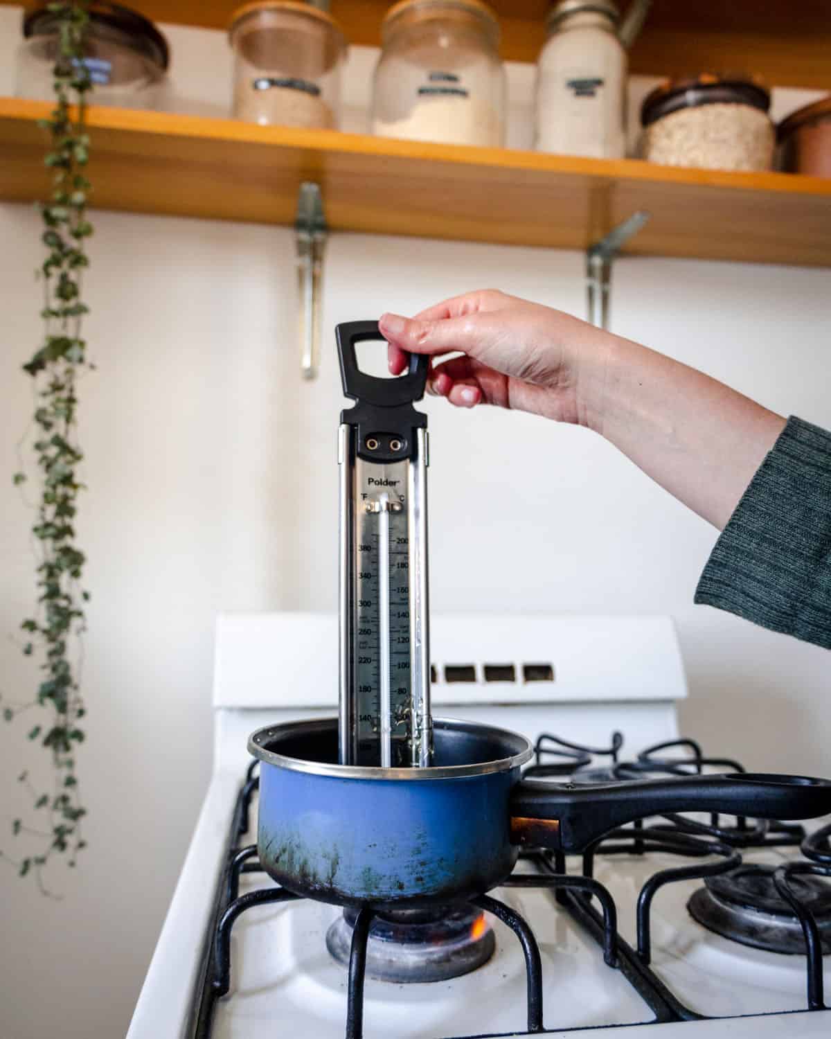 A pot on the stove with a candy thermometer in it. 