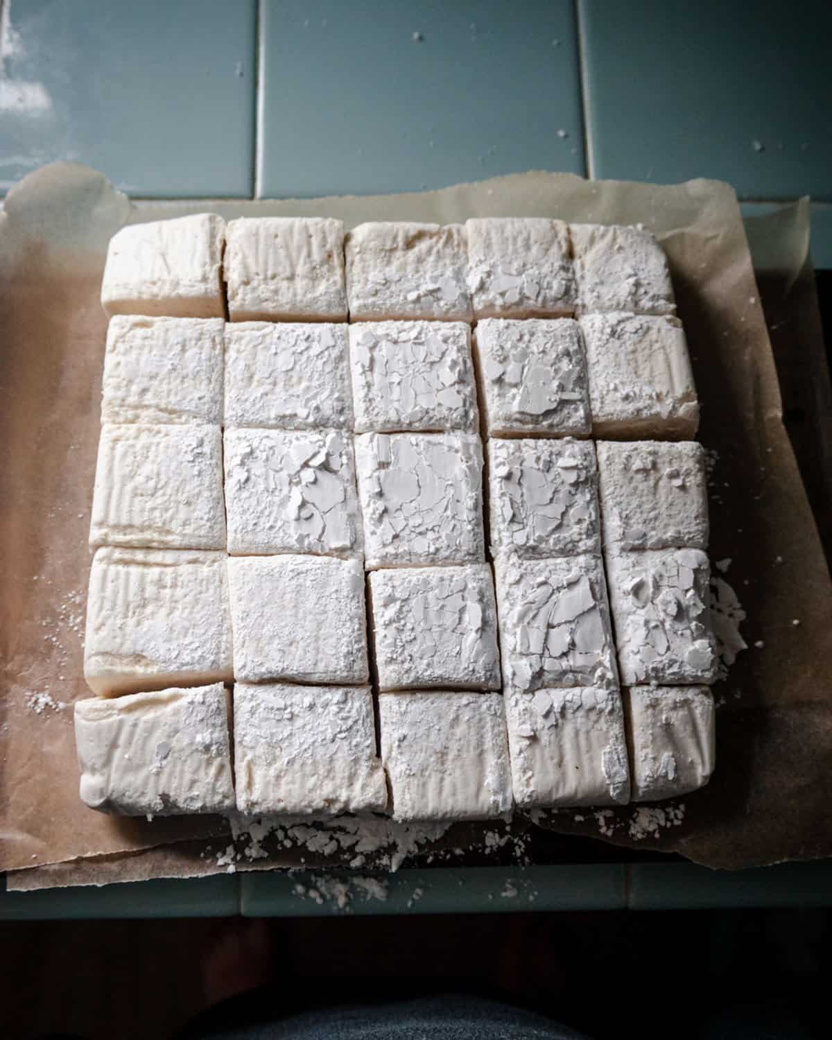 A pan of marshmallows turned onto a cutting board and completely cut into squares. 