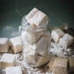 A jar filled with homemade marshmallows and surrounded by other homemade marshmallows.