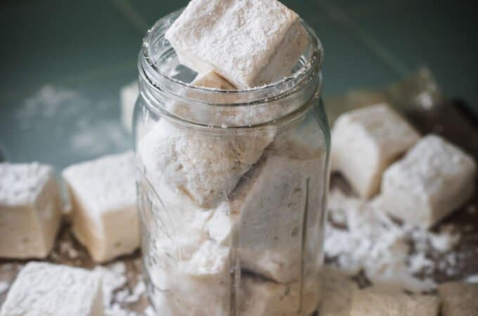 A jar filled with homemade marshmallows and surrounded by other homemade marshmallows.