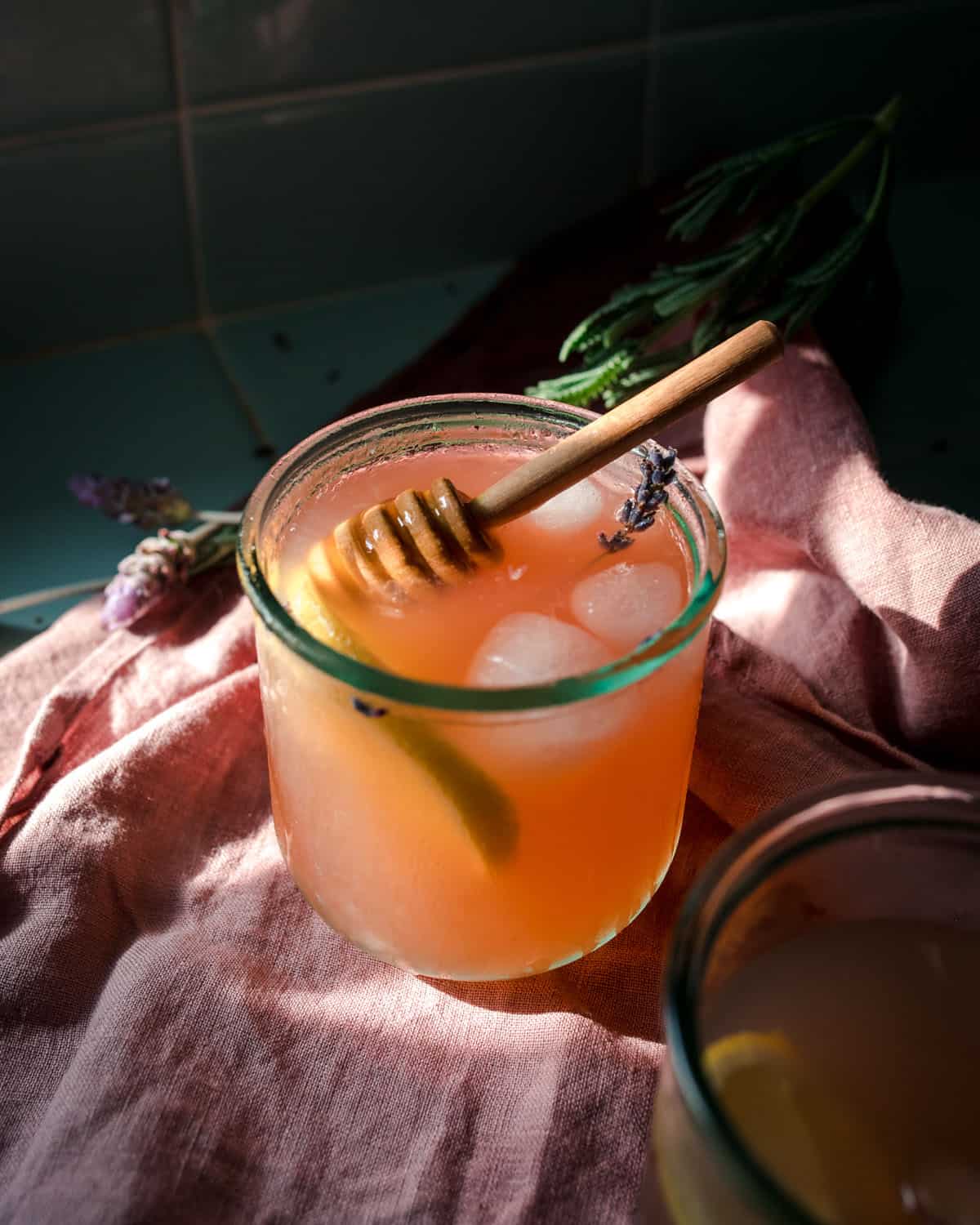 A glass of lavender lemonade with a honey stick. 