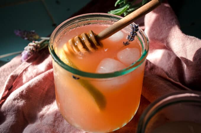 A glass of iced lavender lemonade with a honey stick in it.