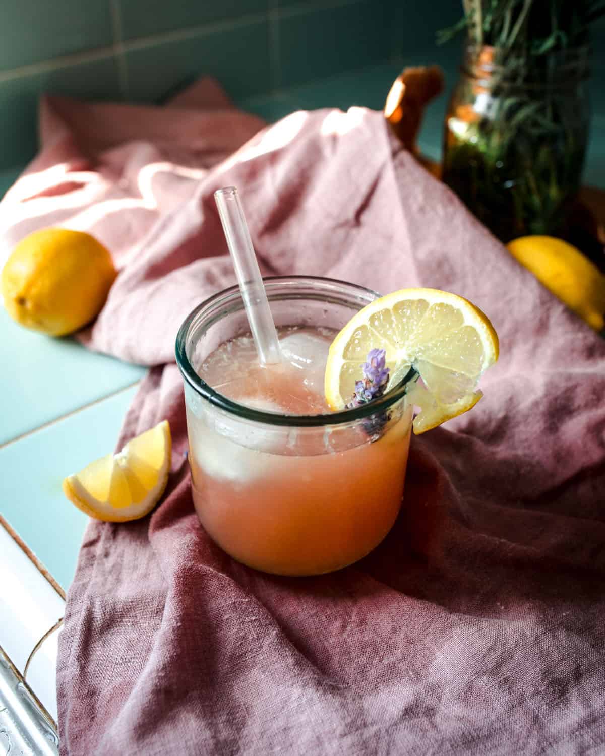 Lavender lemonade in a glass with a glass straw and a slice of lemon on the edge. 