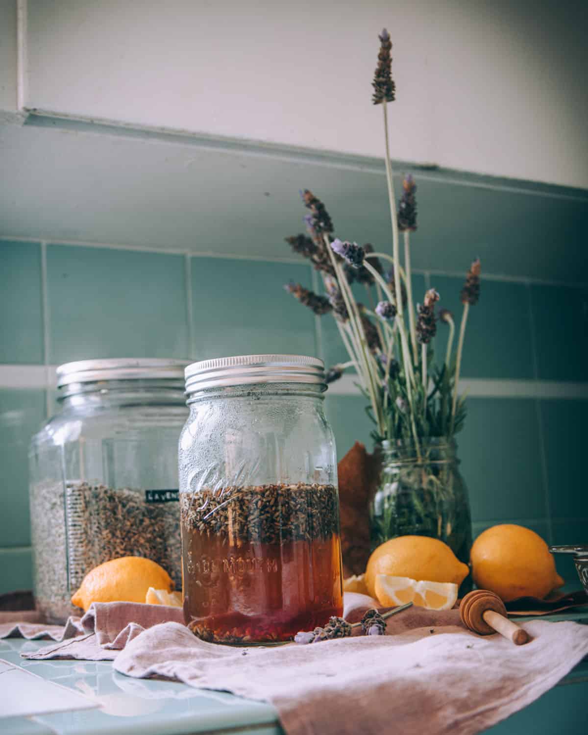 Lavender tea steeping in a jar, with lemons and fresh lavender surrounding. 