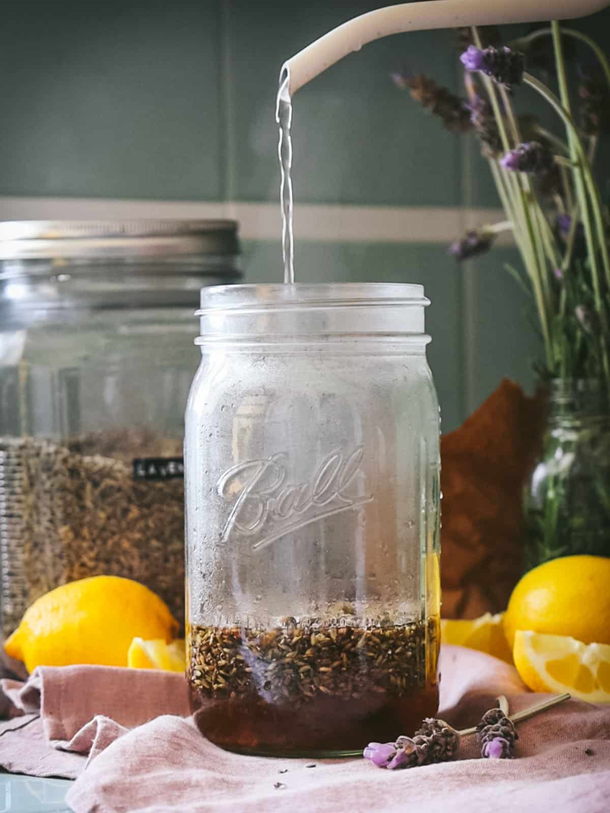 Boiling water pouring over dried lavender in a jar, with lemons surrounding. 