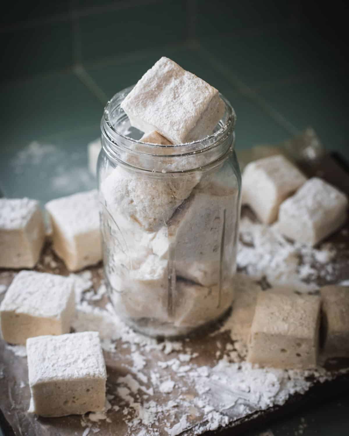 Marshmallows in a jar, with other marshmallows scattered around. 