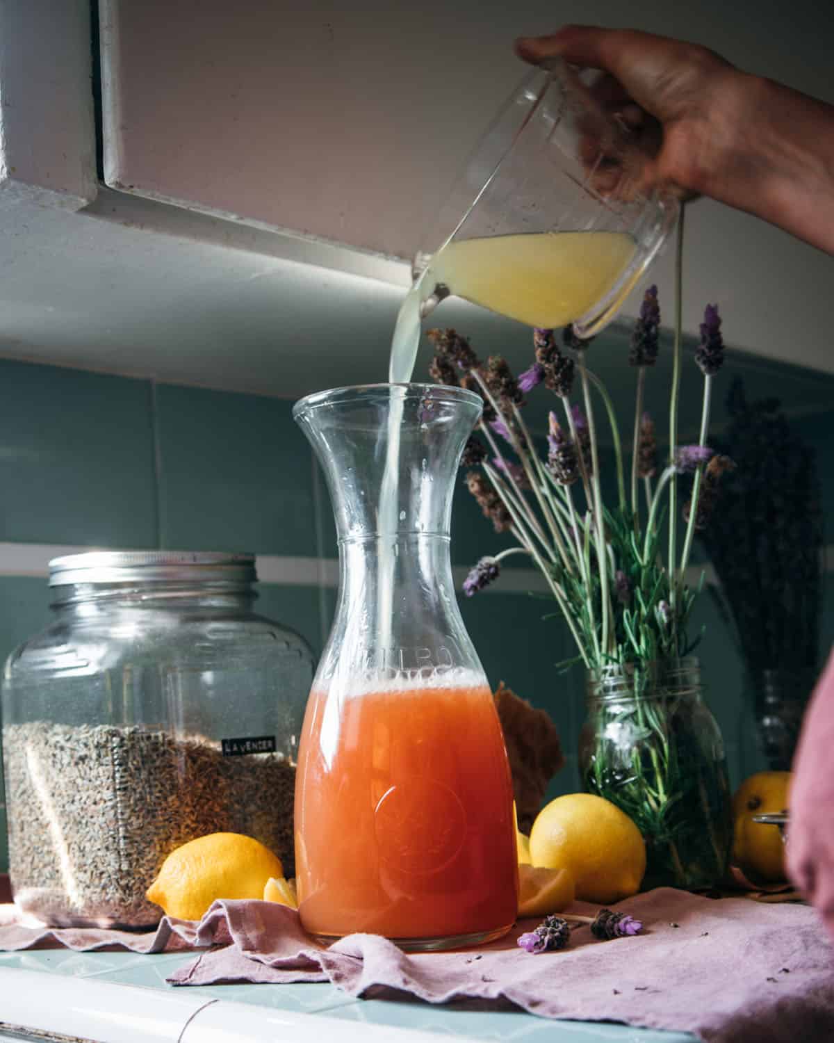 Lemon juice pouring into the lavender tea, surrounded by fresh lemons and lavender. 