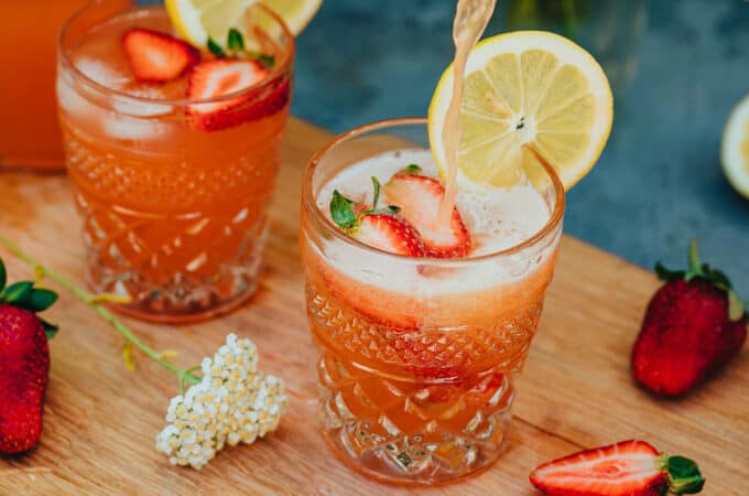 2 glasses of yarrow rose soda, topped with fresh sliced strawberries and lemons.