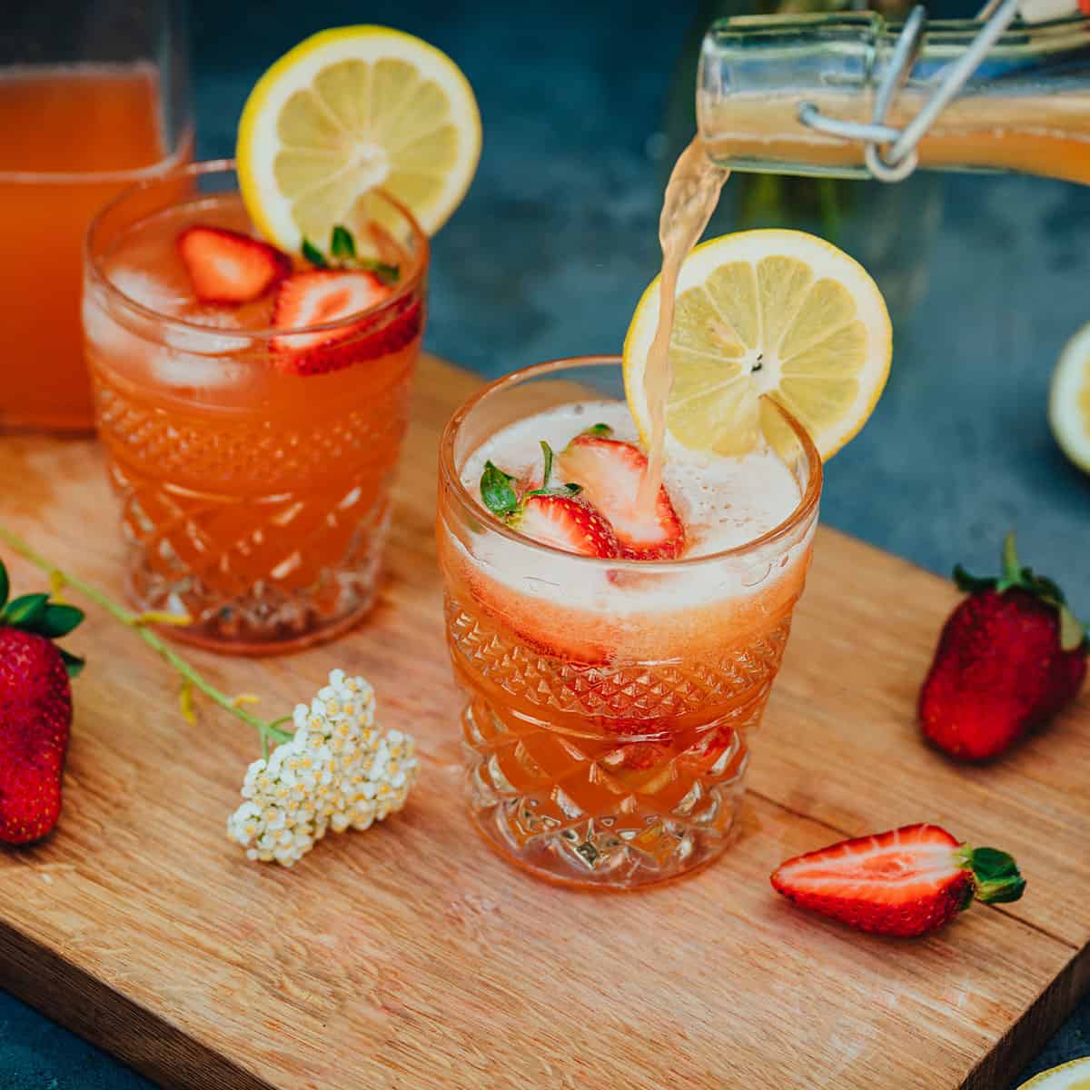 2 glasses of yarrow rose soda, topped with fresh sliced strawberries and lemons.