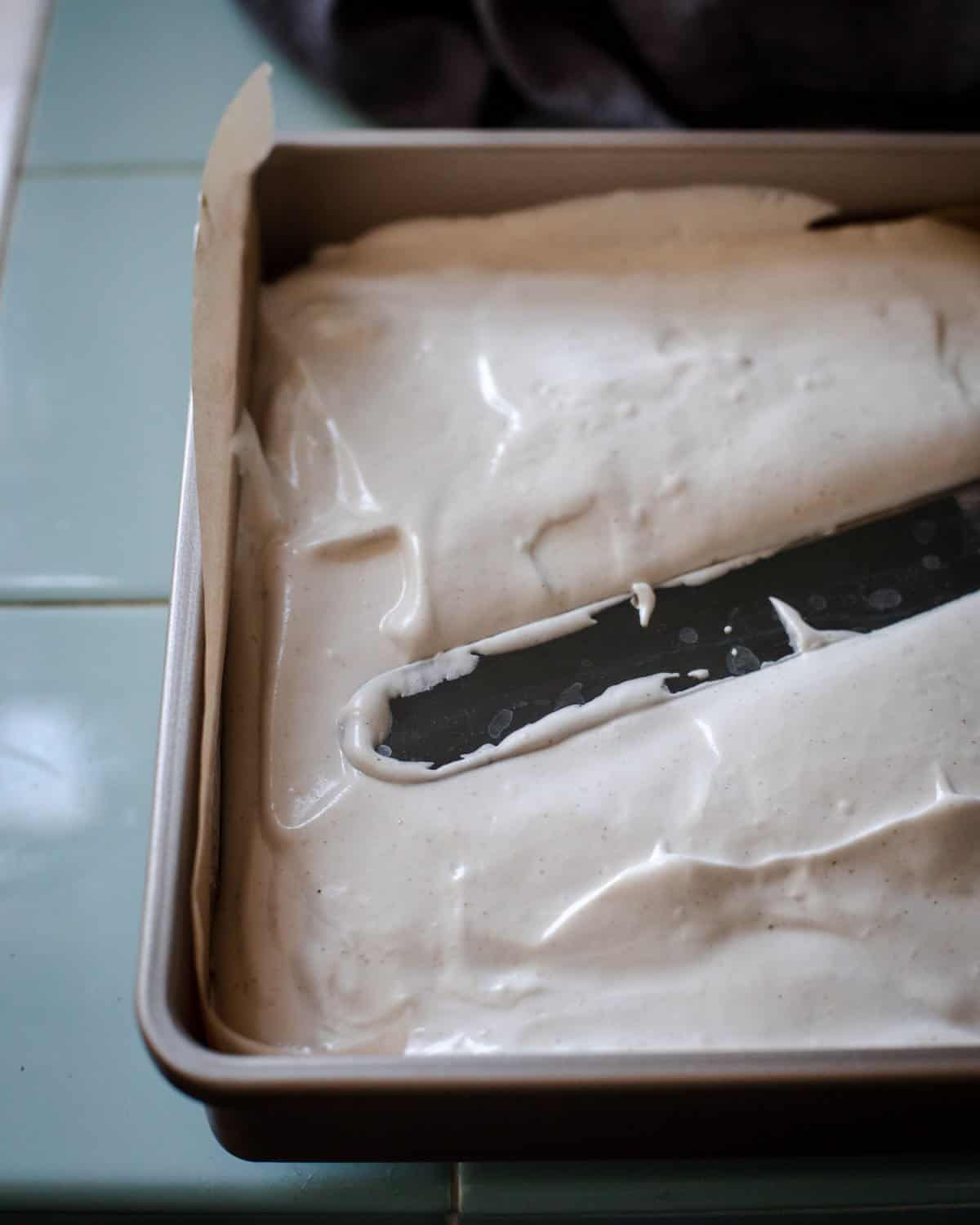 A pan of marshmallow fluff being spread flat with a spatula. 