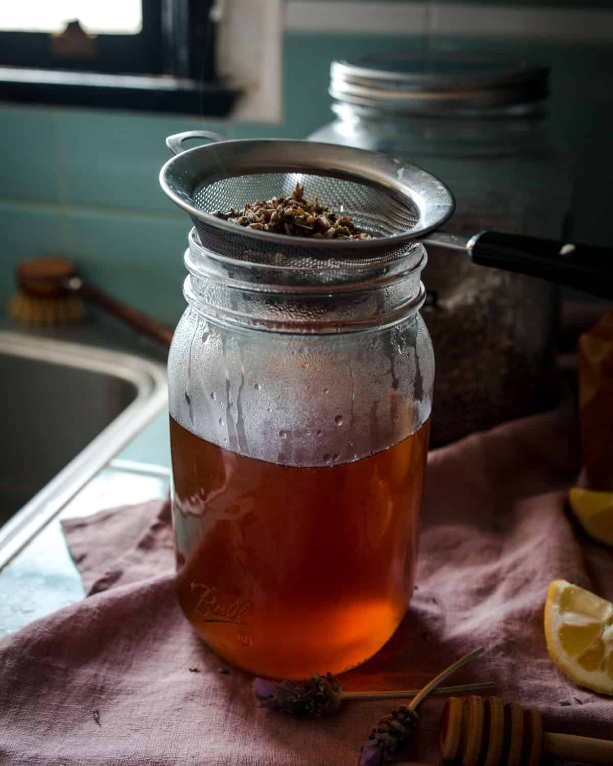 A jar of tea with a strainer on top with spent lavender tea flowers. 