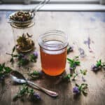 A jar of self-heal oxymel surrounded by self-heal flowers.