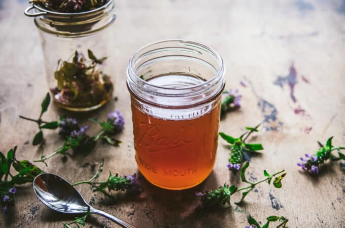 A jar of self-heal oxymel surrounded by self-heal flowers.