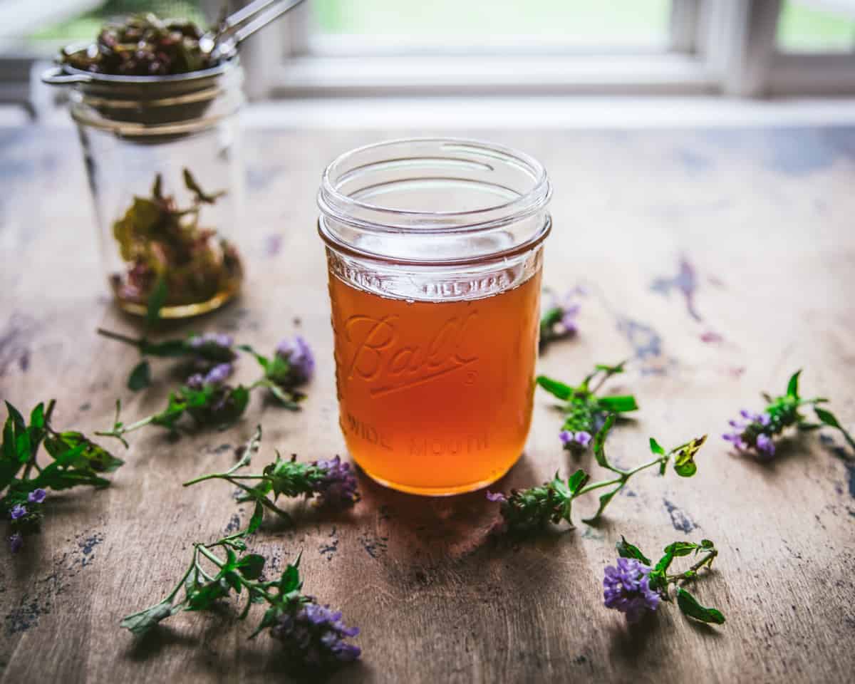 Self-heal oxymel in a jar surrounded by self-heal flowers. 