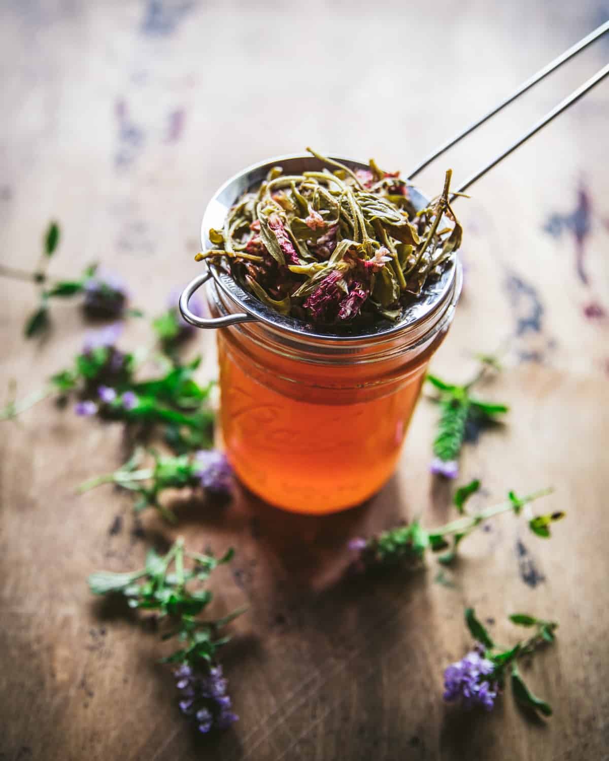 Oxymel in a jar with a strainer filled with spent self-heal flowers resting on top.