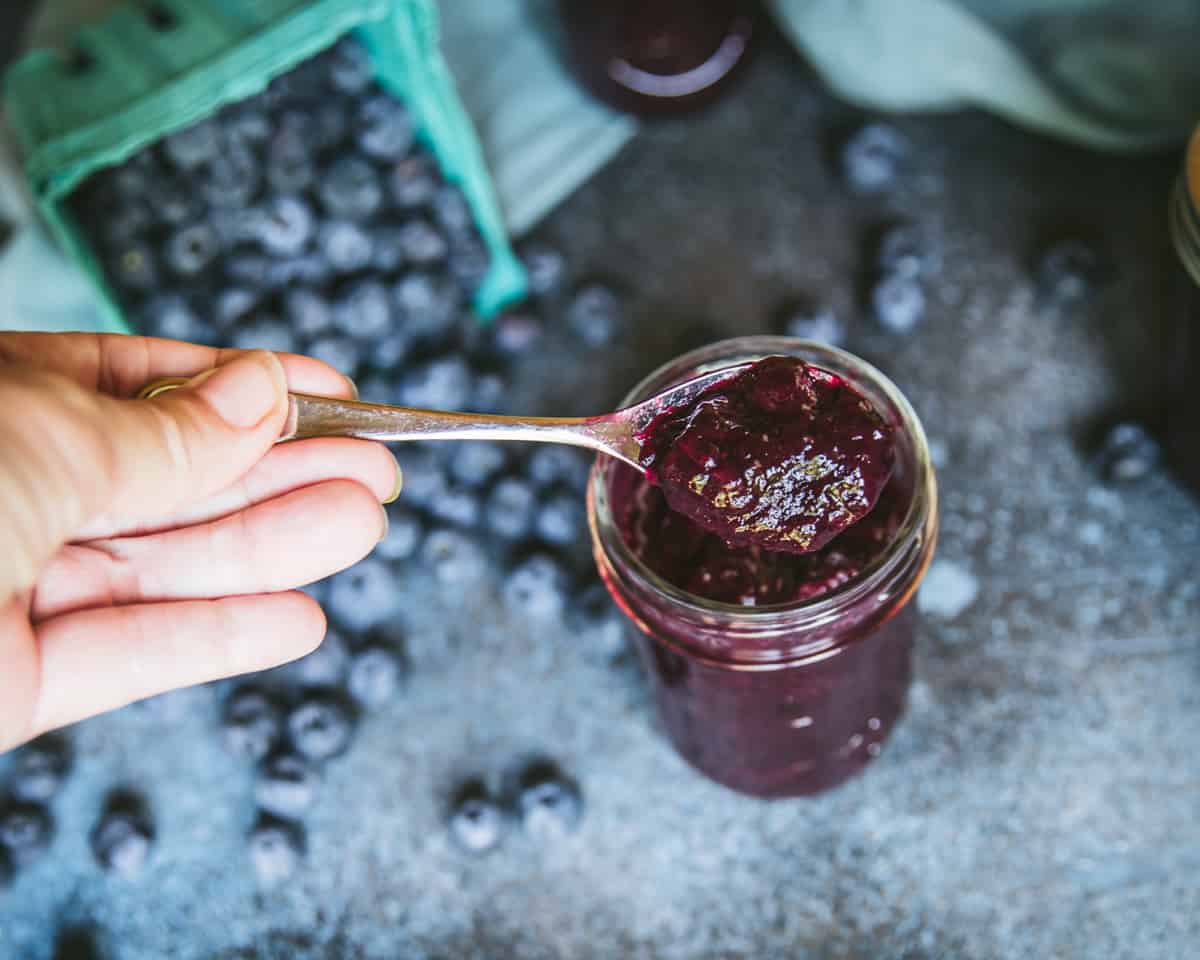 Blueberry jam on a spoon lifting out of a jar. 