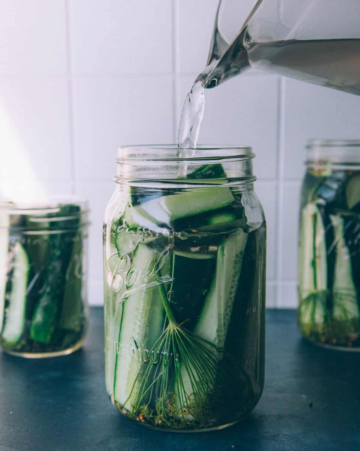 Pitcher of saltwater brine pouring over the cucumbers and spices. 