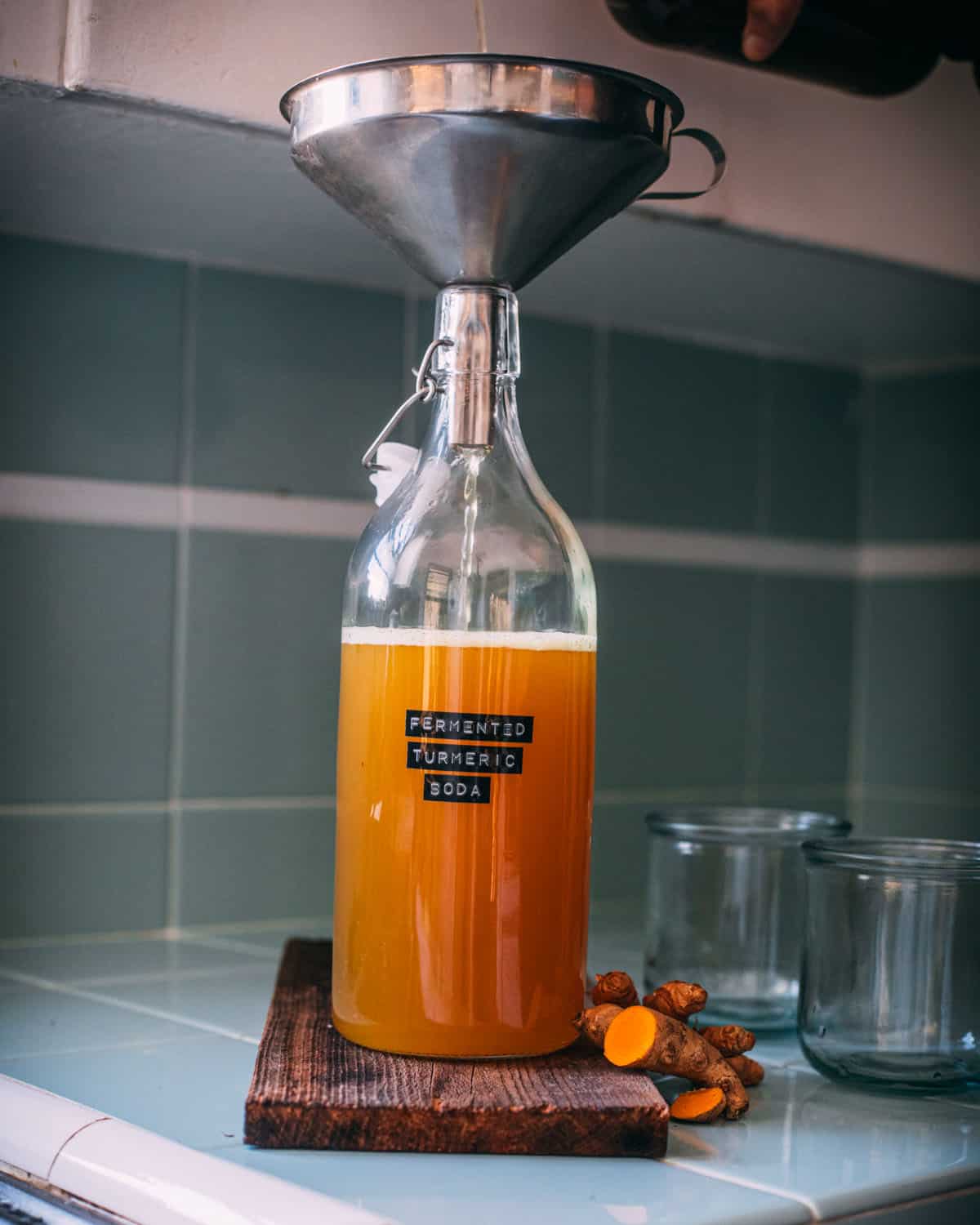 Turmeric soda pouring into a flip top bottle through a funnel. 