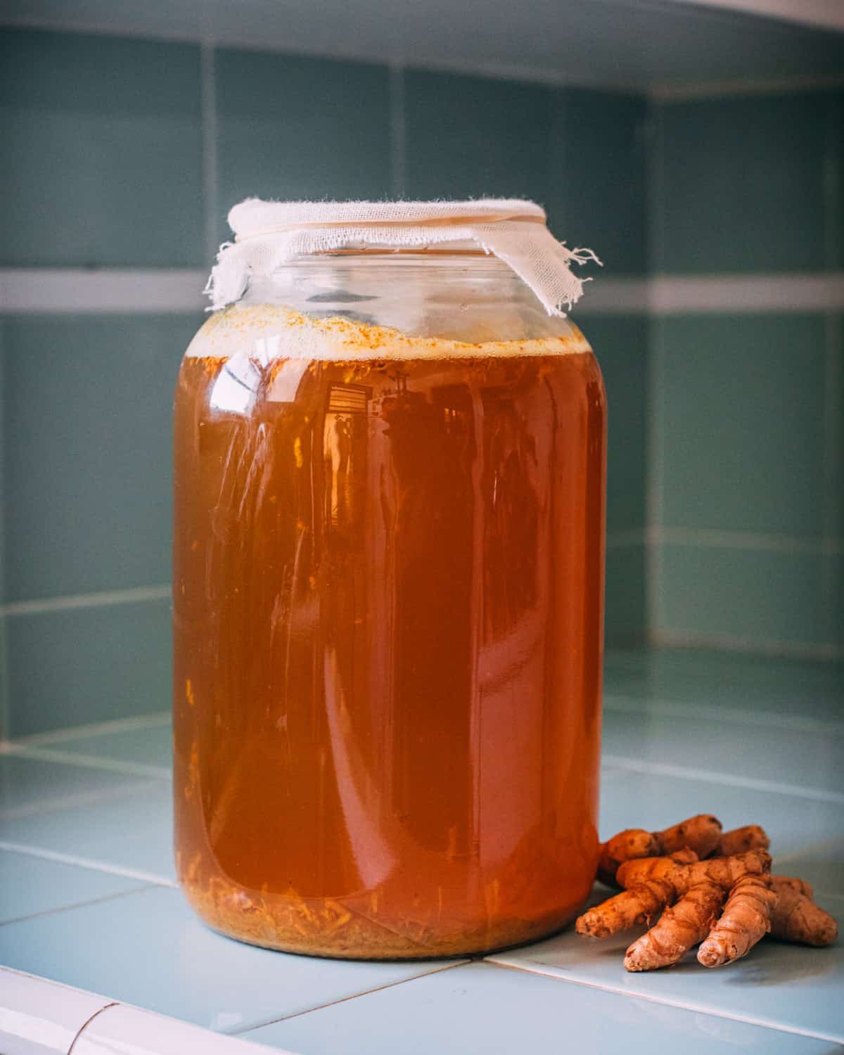 A gallon size jar of turmeric soda with cheesecloth on top.