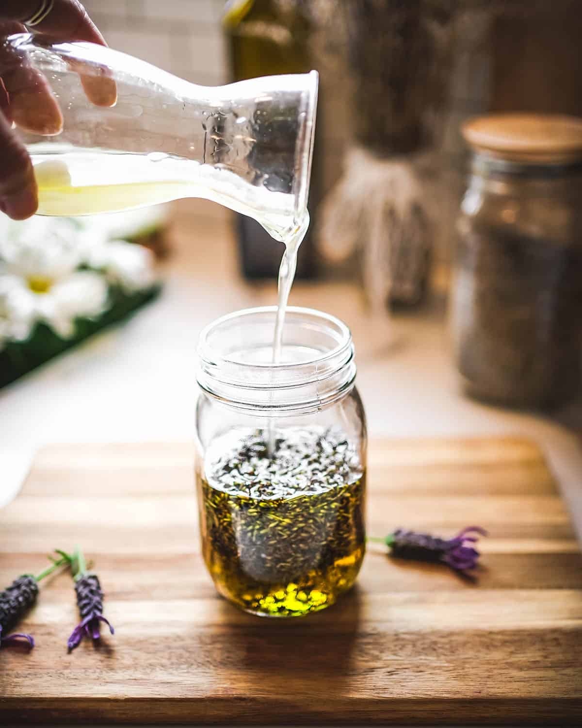 Oil pouring into a jar with dried lavender buds. 