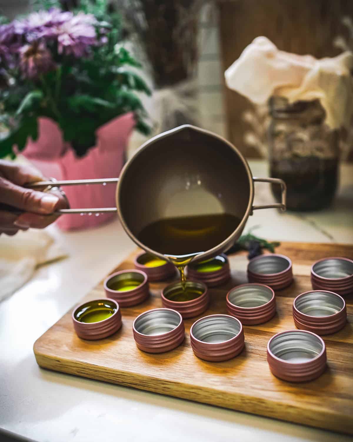 Melted salve pouring into tins with a measuring cup.