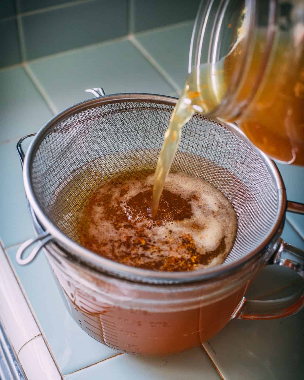 Turmeric soda being poured into a glass jar through a mesh strainer.