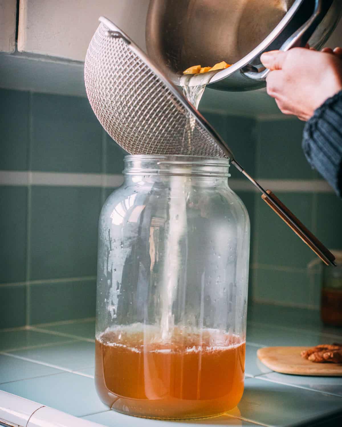 Straining the spices out of the soda from the pan, pouring into a glass jar. 