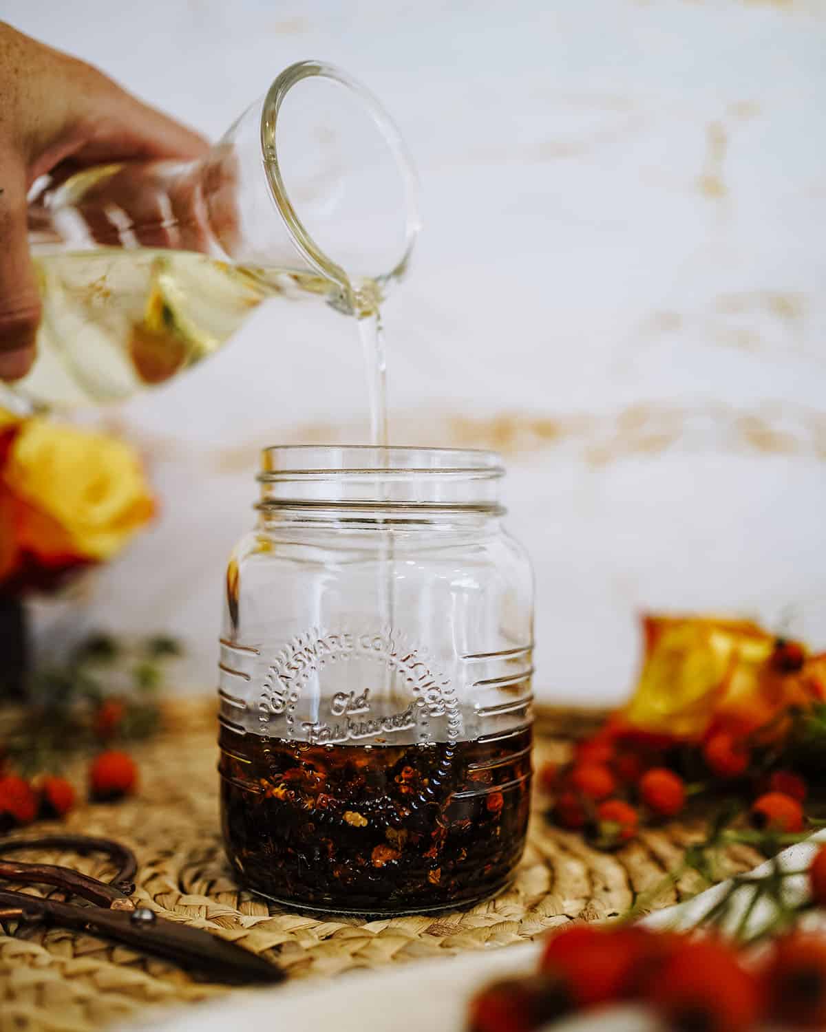 Oil pouring into the jar with the dried rose hips. 