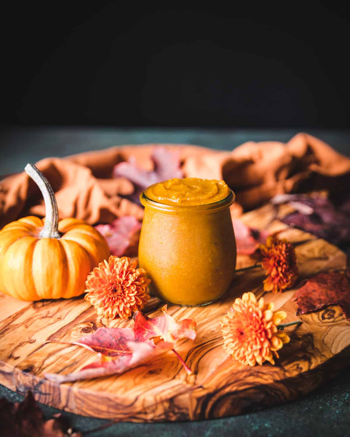 Pumpkin butter in a jar surrounded by fall leaves and flowers. 