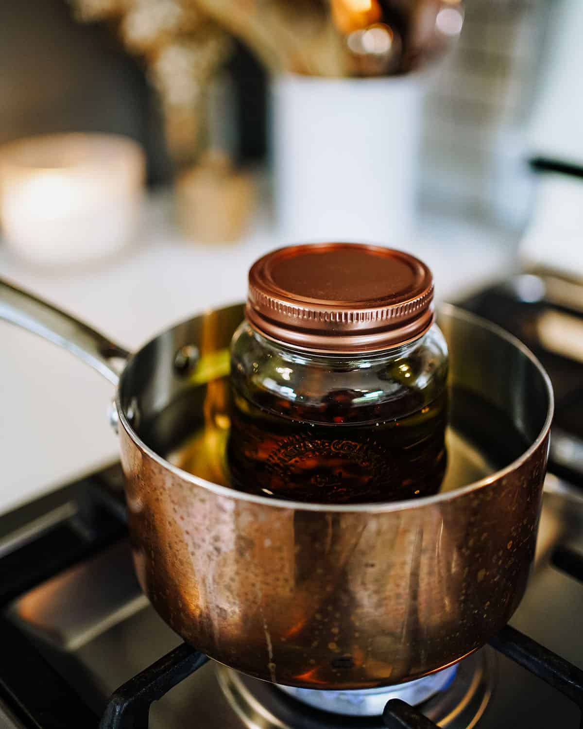 The jar of oils mixed with dried rose hips is sitting in a pot of water on the stove on low heat to simmer, with the lid of the jar on. 
