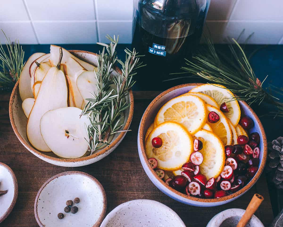 Bowls of fresh garnish for mulled wine, including orange slices, pear slices, and cranberry. 