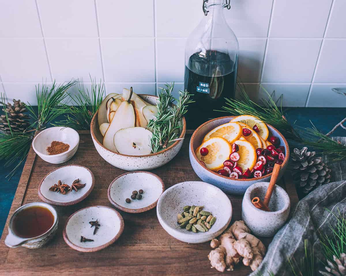 A bottle of red wine with small bowls of spices and fresh garnishes.