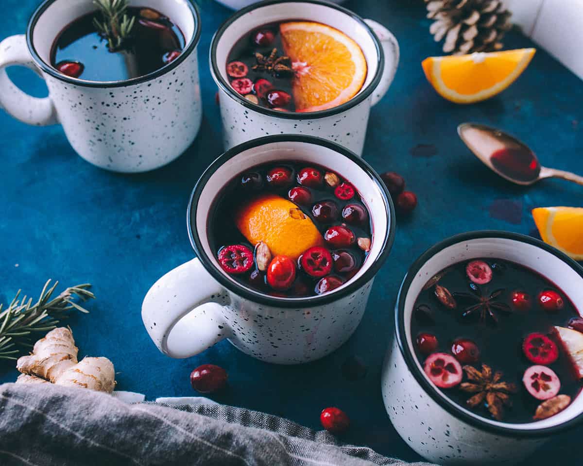 Mugs of mulled wine with garnishes on a dark background.