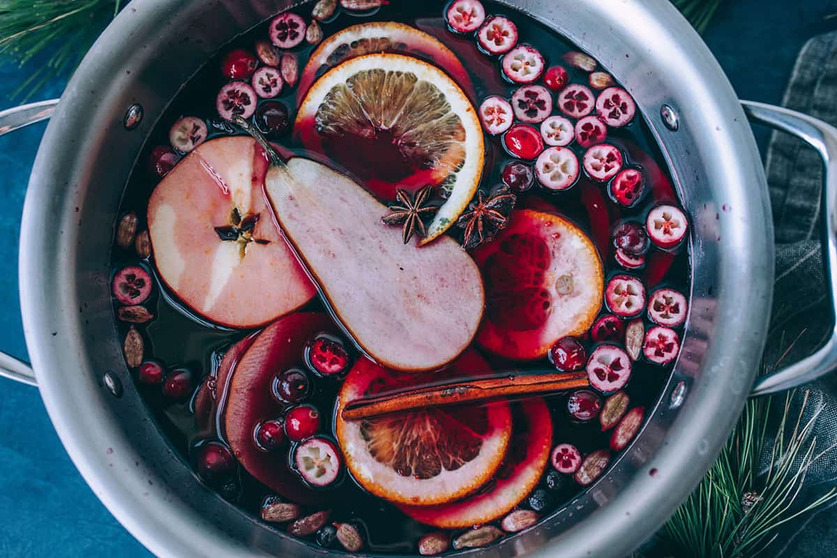 Mulled wine in a large pot, with mulling spices and garnishes floating on the top.