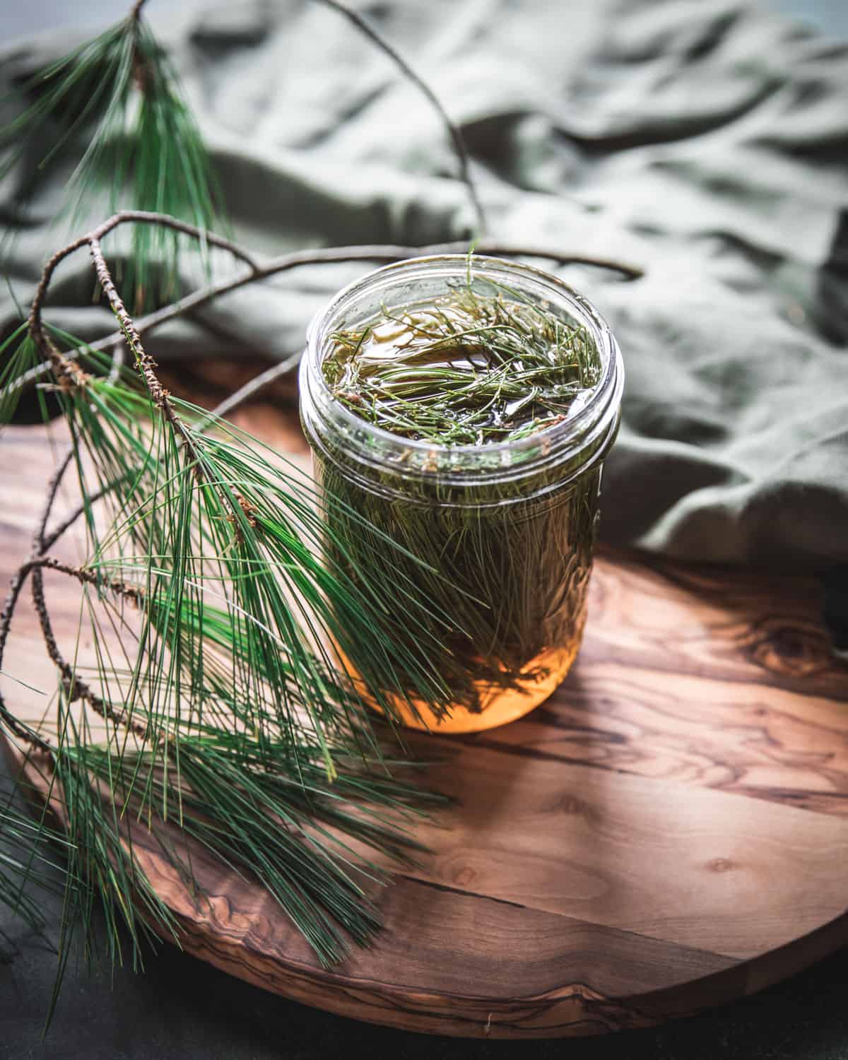 A jar filled with pine needles and honey surrounded by fresh pine needles.