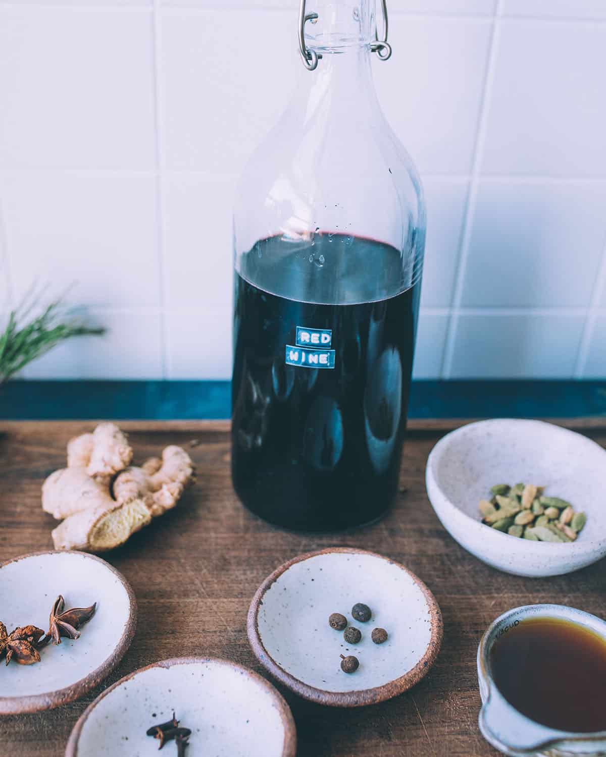 A clear bottle of red wine and mulling spices measured out into small bowls surrounding. 